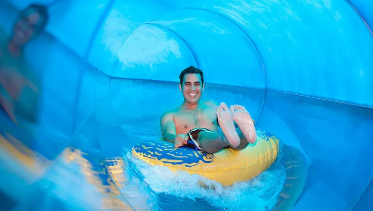 A man smiles at the camera as she rides a tube down a water slide at a Great Wolf Lodge indoor water park.